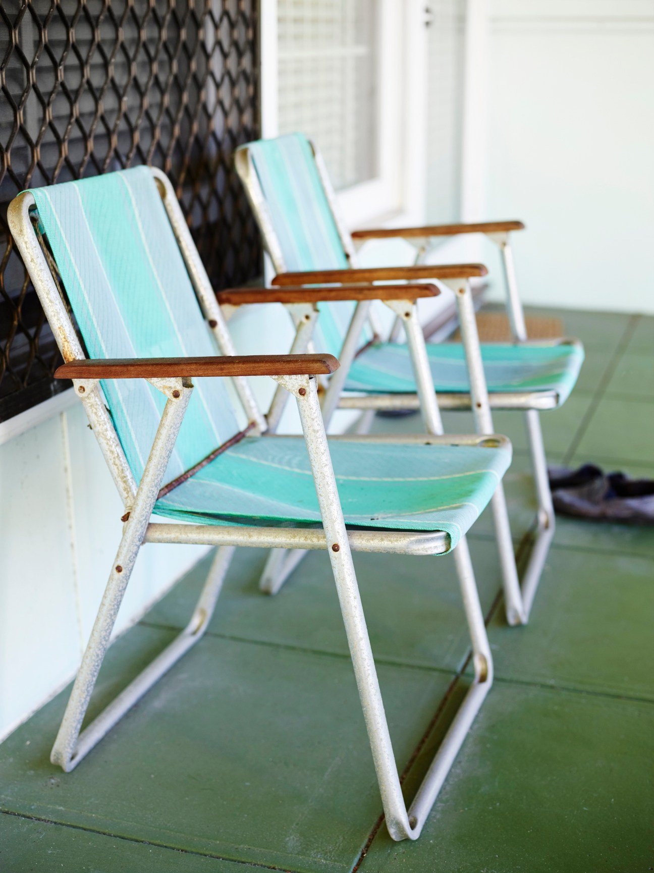 Vintage turquoise and white striped beach chairs with wooden armrests arranged on a green deck.