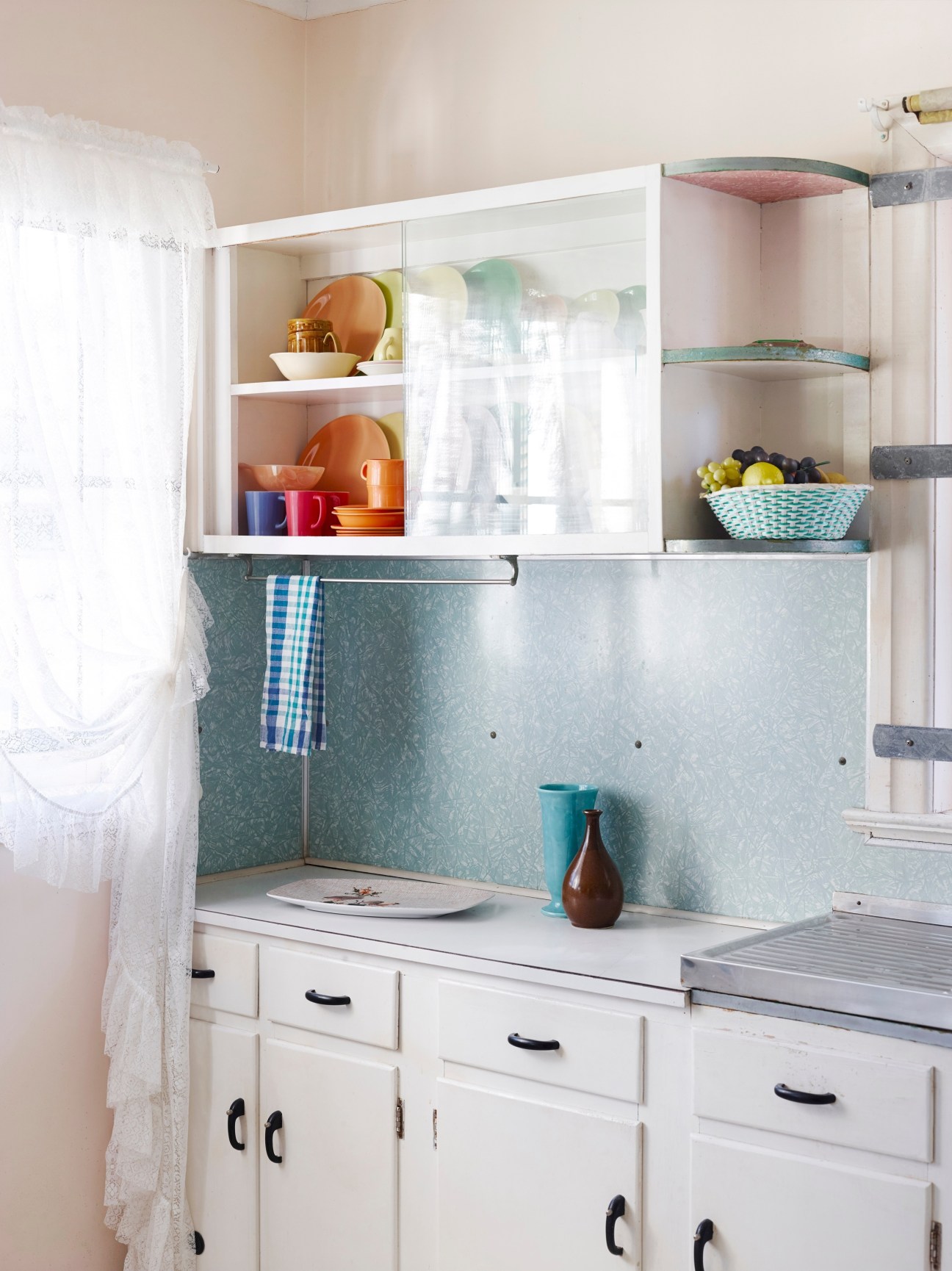 Retro 1950s kitchen with turquoise tile backsplash, white cabinetry, and vintage dishware displayed in open shelving.