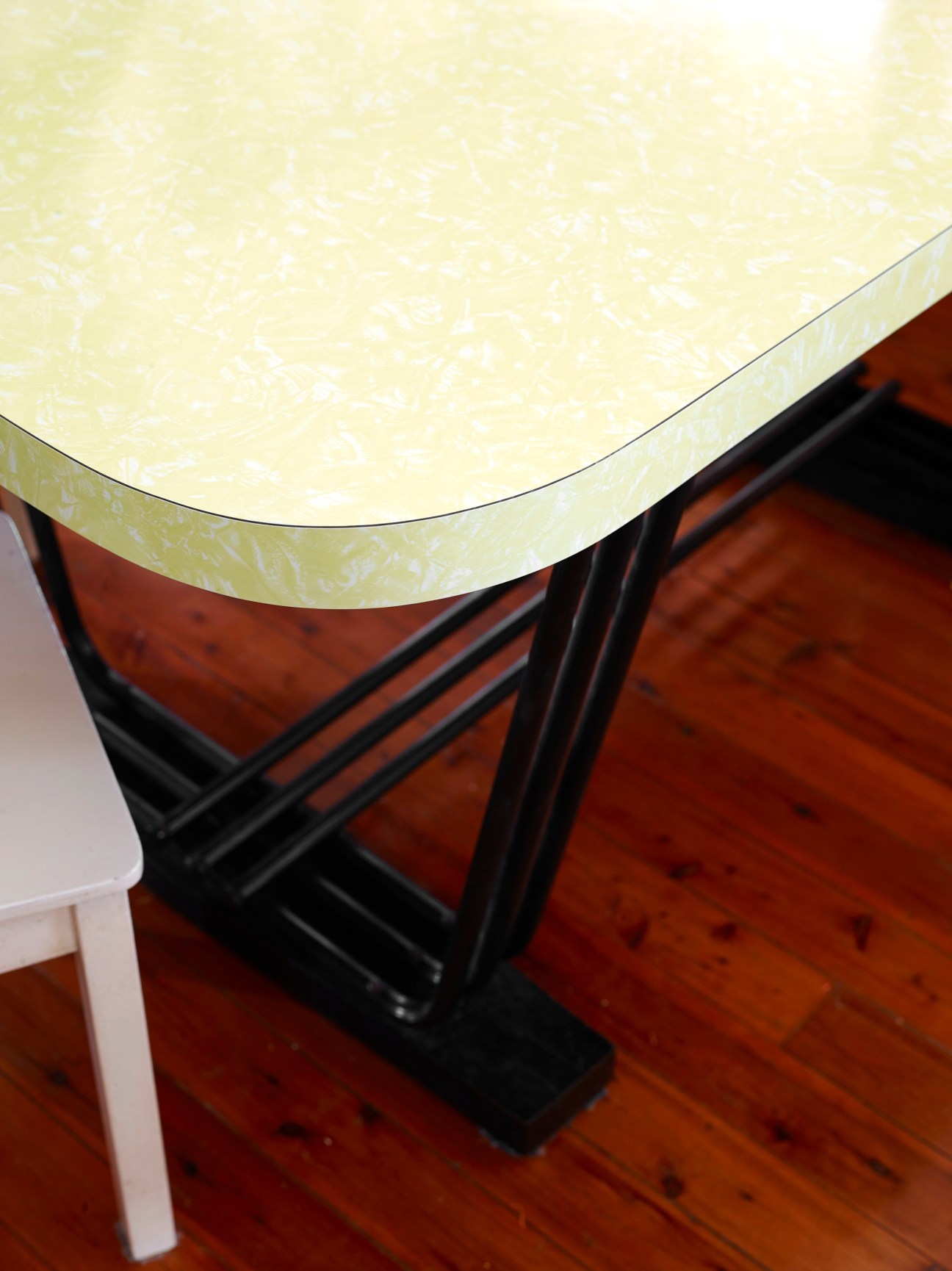 Close-up of a mid-century modern table with pale yellow top and black legs on wooden flooring.