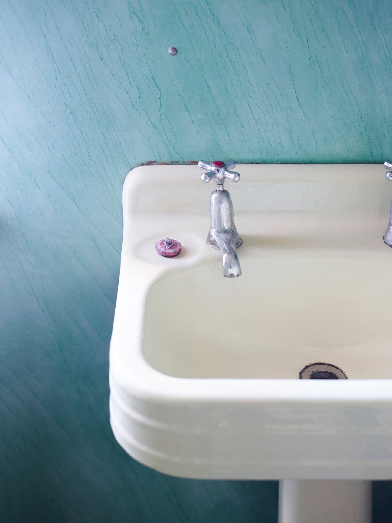 Vintage pedestal sink with chrome tap against turquoise textured wall in a mid-century beach bungalow bathroom.