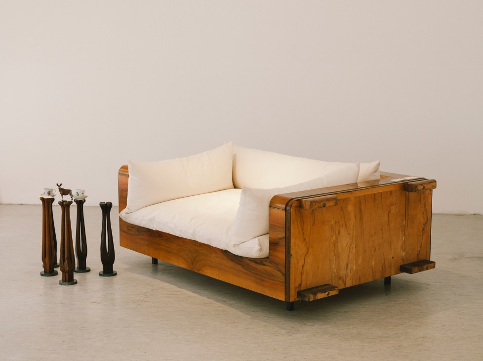 Wooden sofa with cream cushions and decorative wooden candlesticks displayed beside it.