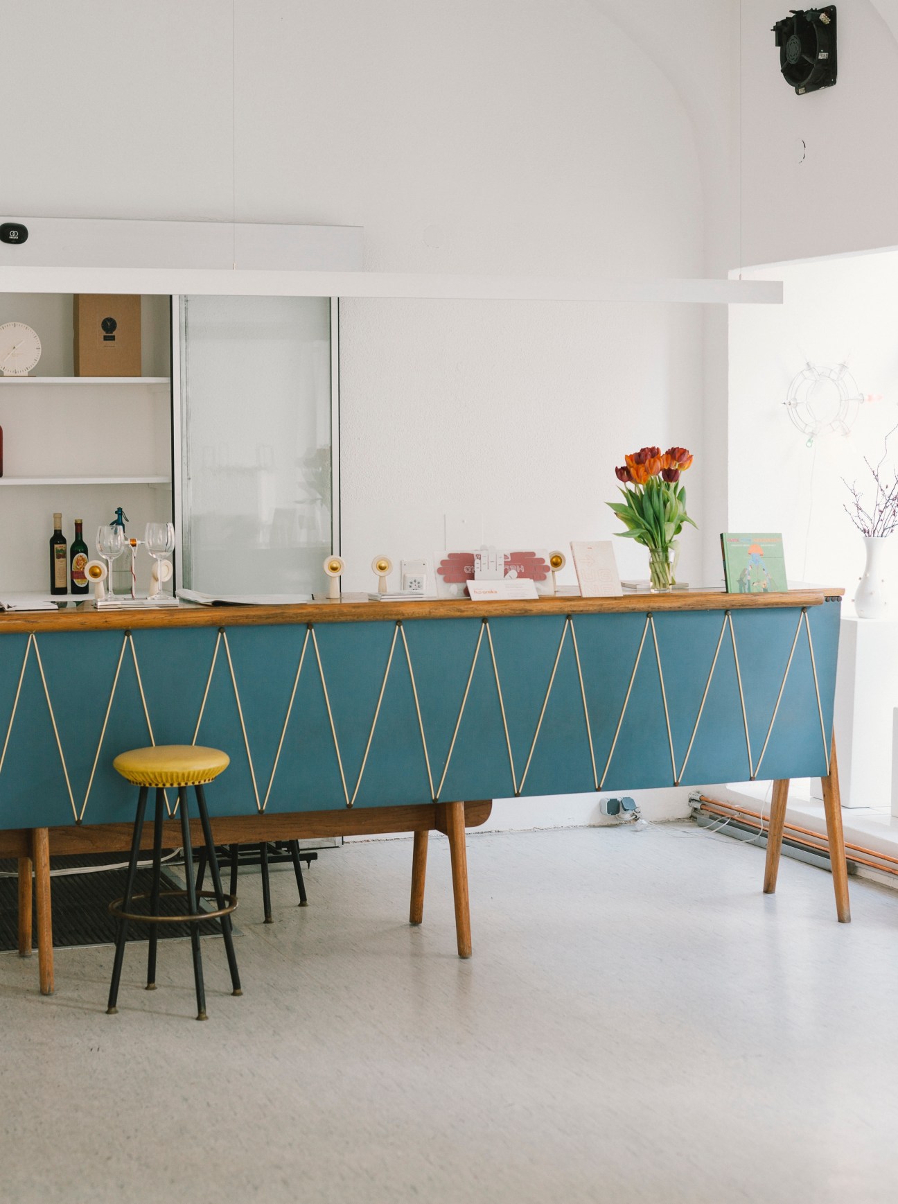 Interior of Himbeer & Soda gallery with teal counter, wooden shelving, and mid-century furniture.