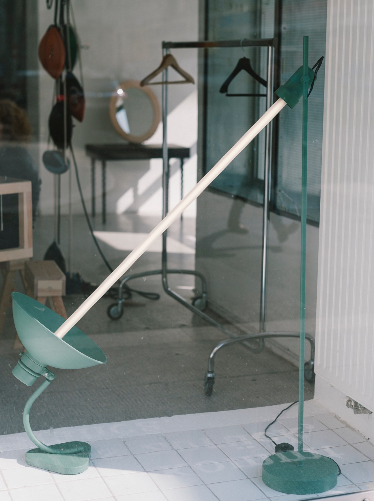 Modern sculptural lamp with teal metal base and white stem displayed in gallery window.