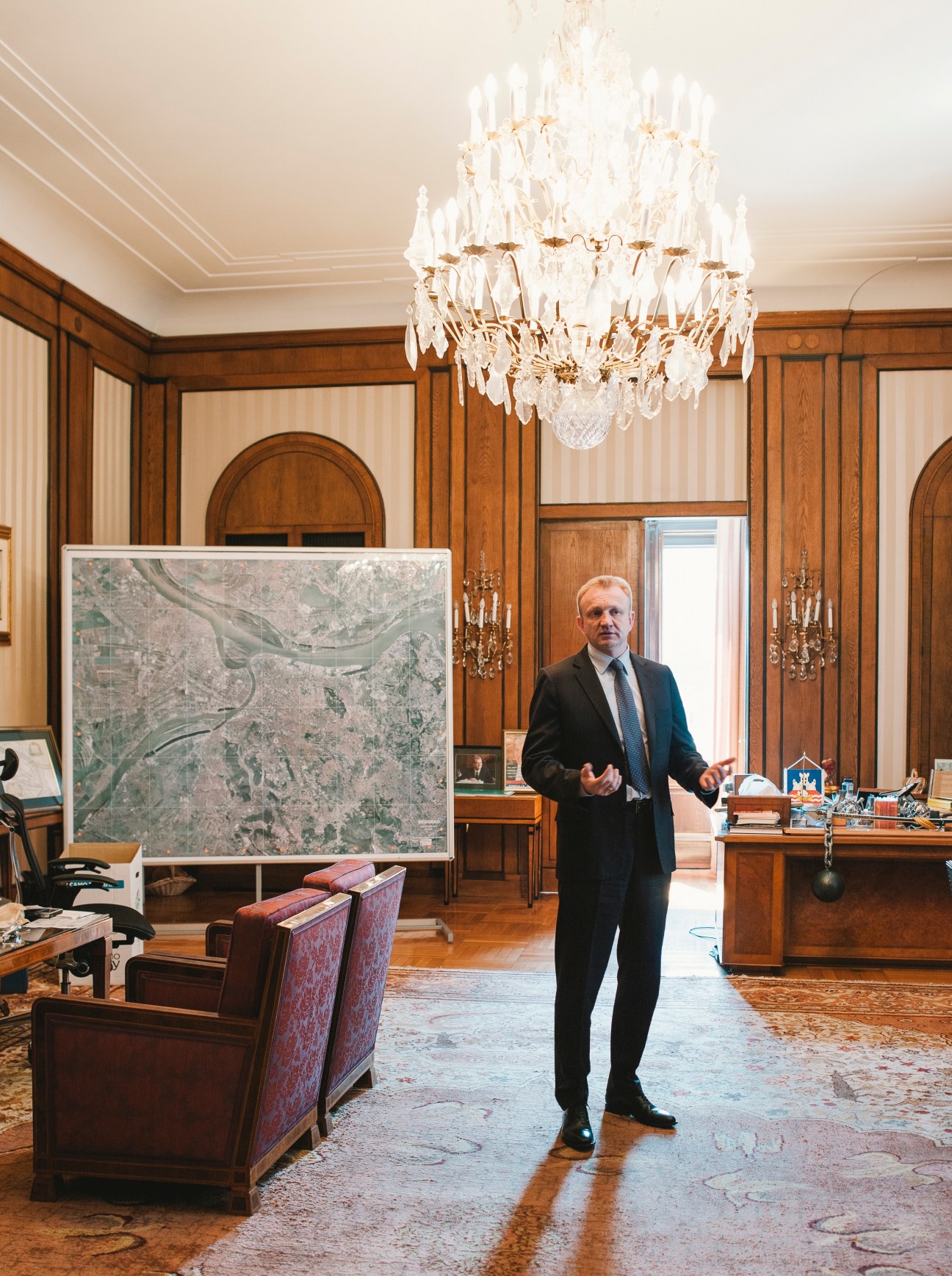 Dragan Djilas, mayor of Belgrade, stands in an ornate wood-paneled office with a crystal chandelier and map on the wall.
