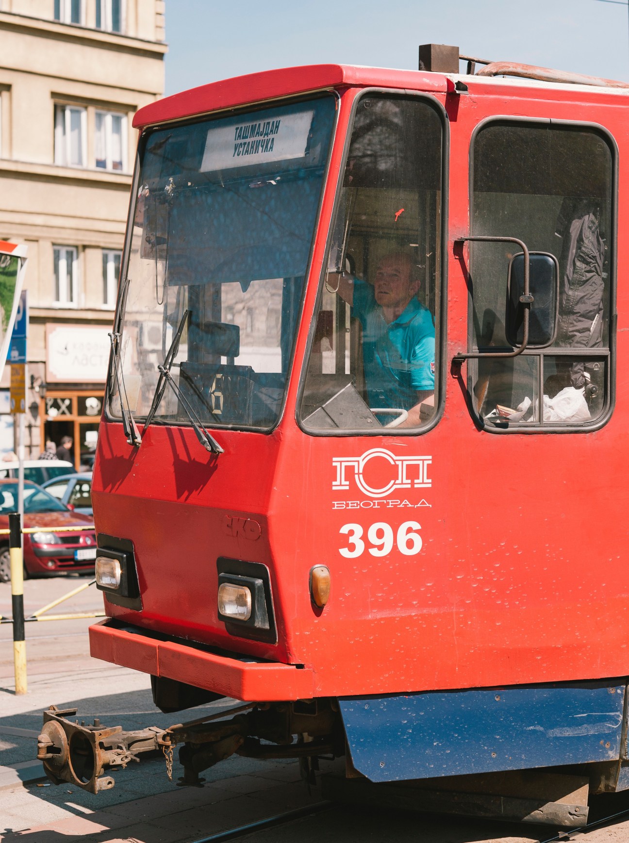 Red and blue Belgrade tram numbered 396 with operator visible in cabin on city street