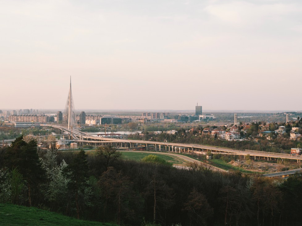 Ada Bridge spanning the Sava river with Belgrade cityscape and surrounding landscape in background.