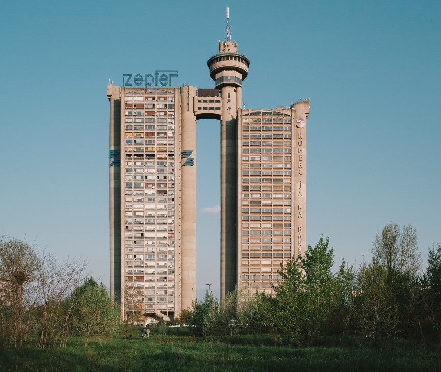 Genex Tower, a massive brutalist structure with twin connected towers and a central observation deck, against a clear blue sky.