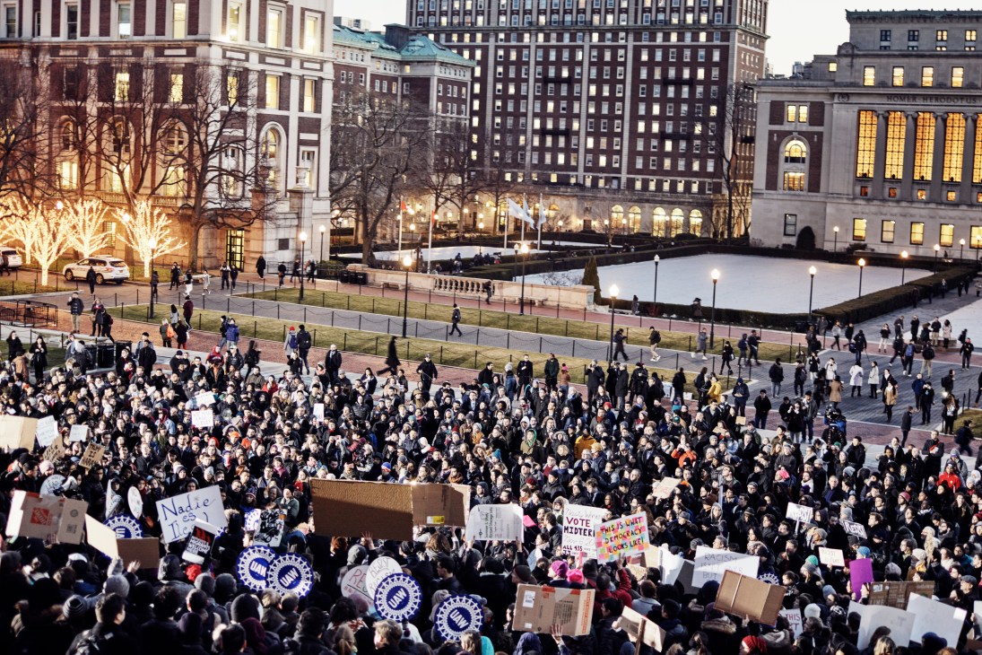 Large crowd of protesters holding signs at Columbia University plaza against Trump's refugee ban executive order.