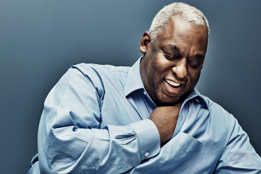 Man in light blue shirt smiling against blue background.
