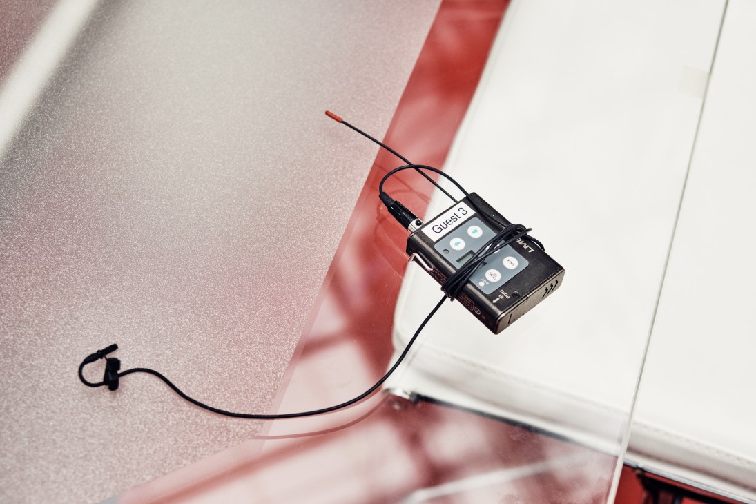 A wireless microphone receiver labeled 'Guest 3' with attached earpiece on a red and white surface.