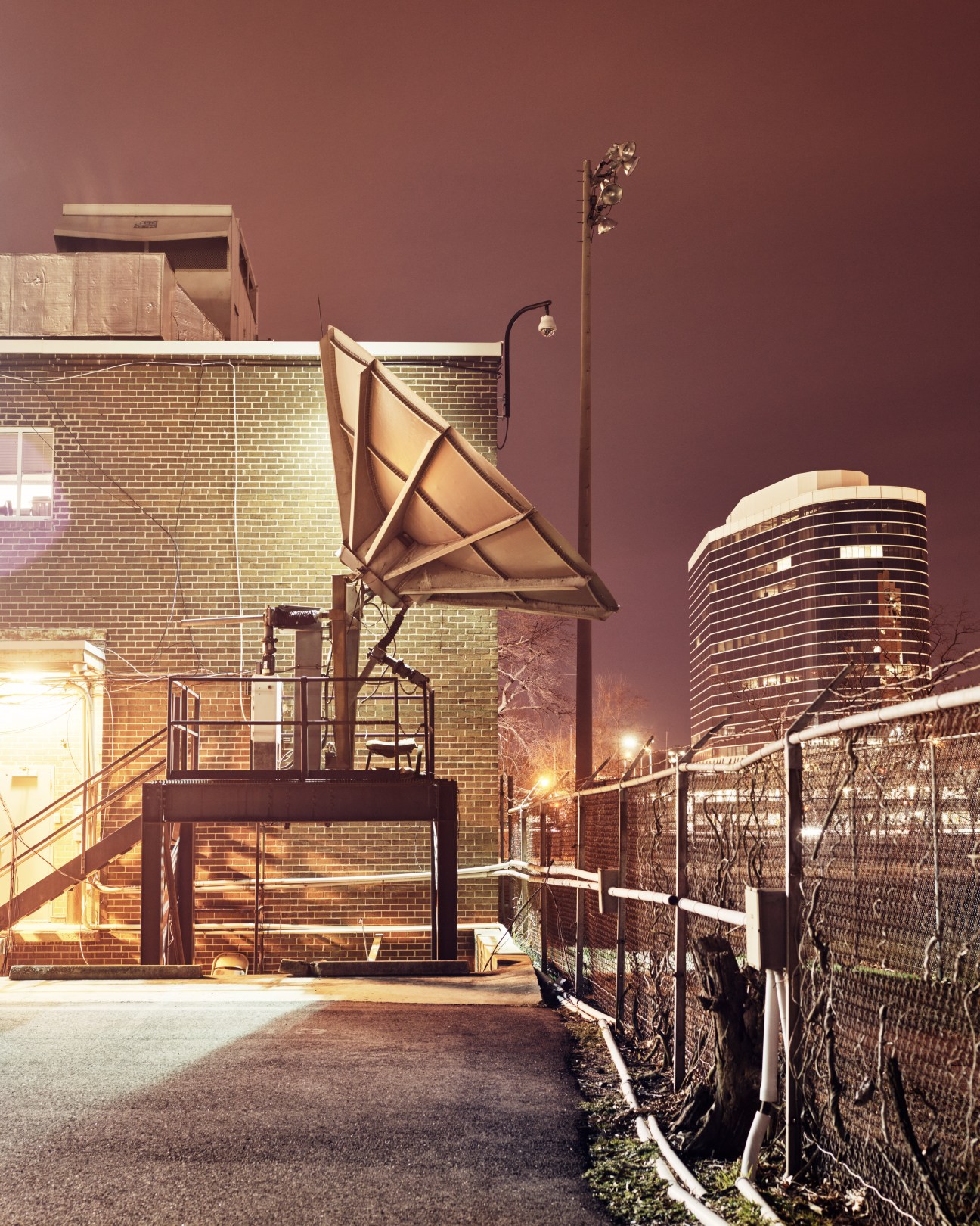Large satellite dish on a brick building rooftop at dusk with modern high-rise in background.