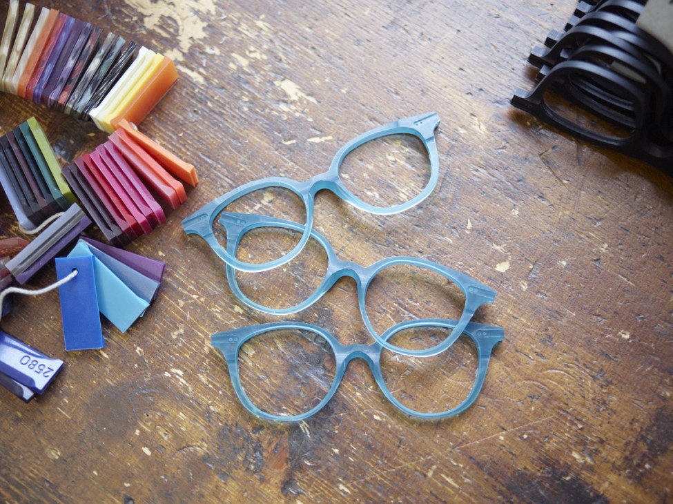 Freshly laser-cut blue eyeglass frames arranged on a wooden surface with colorful acetate sample swatches.