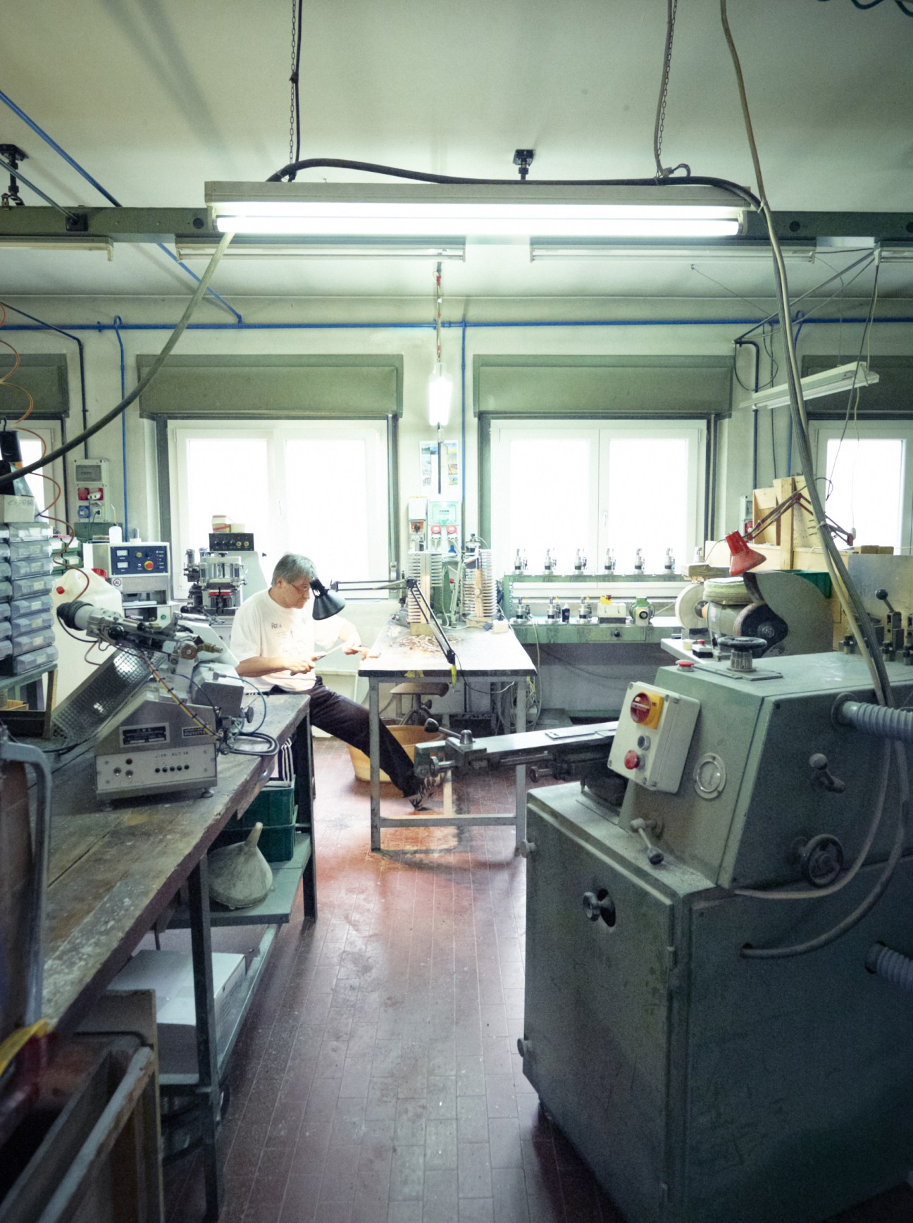 Interior of Kador eyewear factory with craftsman working at workbench surrounded by machinery and tools.