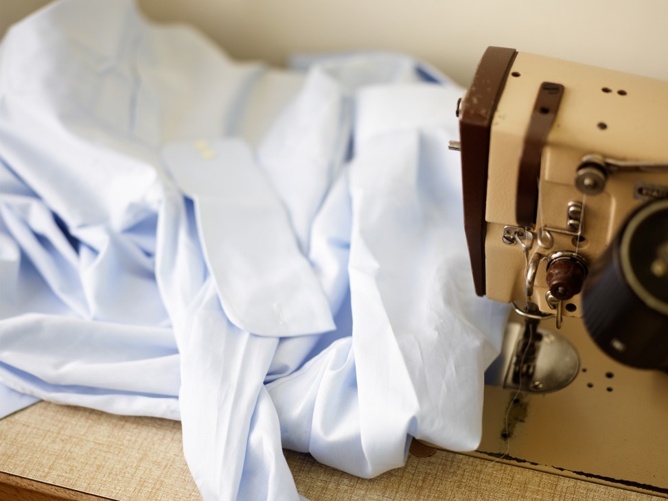 Vintage sewing machine with leather straps and cream-colored fabric being altered.