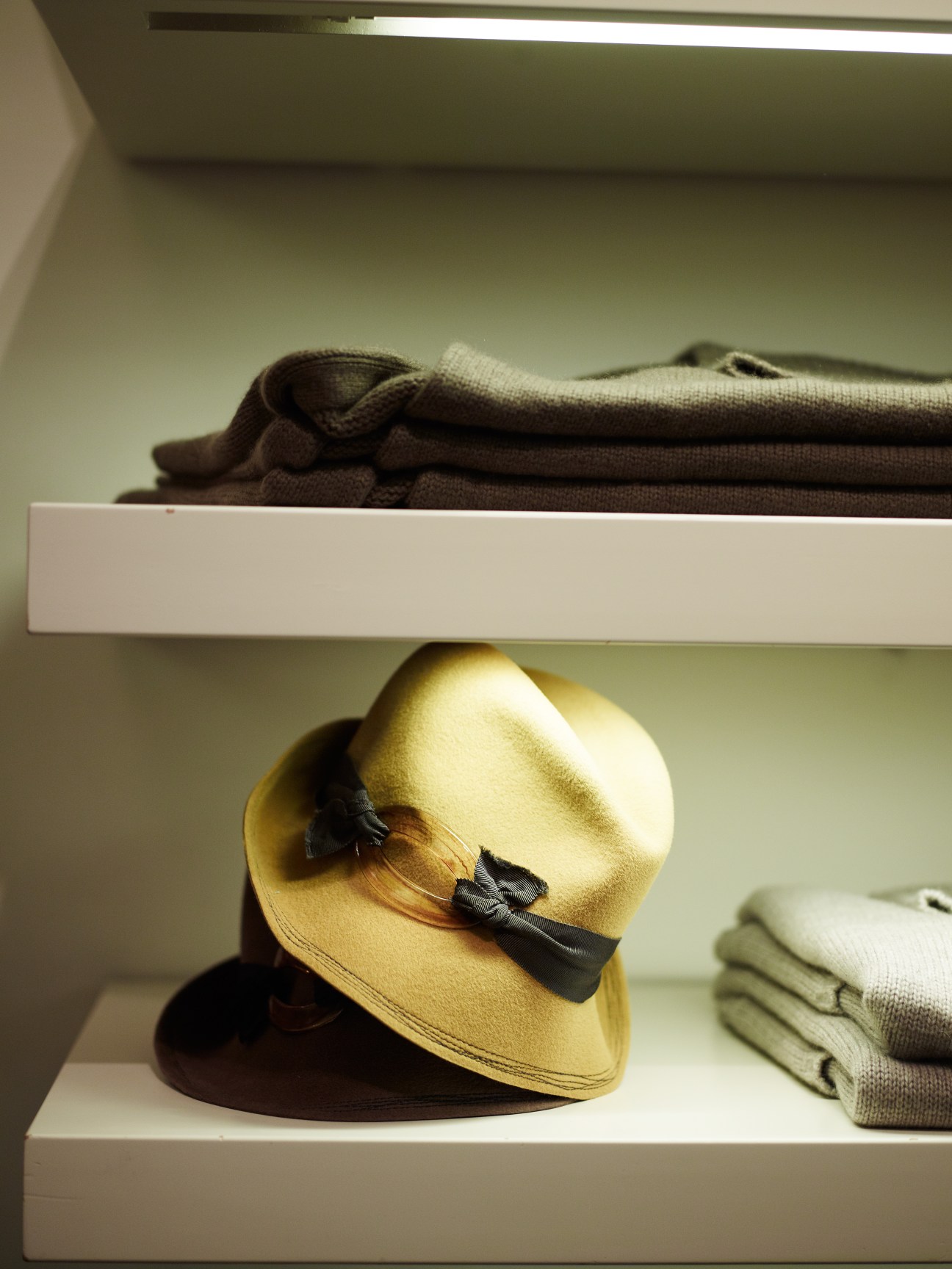Yellow hat with black bow displayed on white shelf alongside folded knitwear.