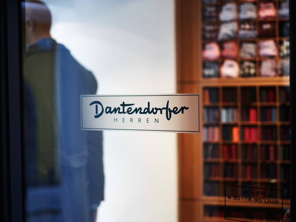 Dantendorfer Herren storefront sign on glass door with wooden display shelves visible behind