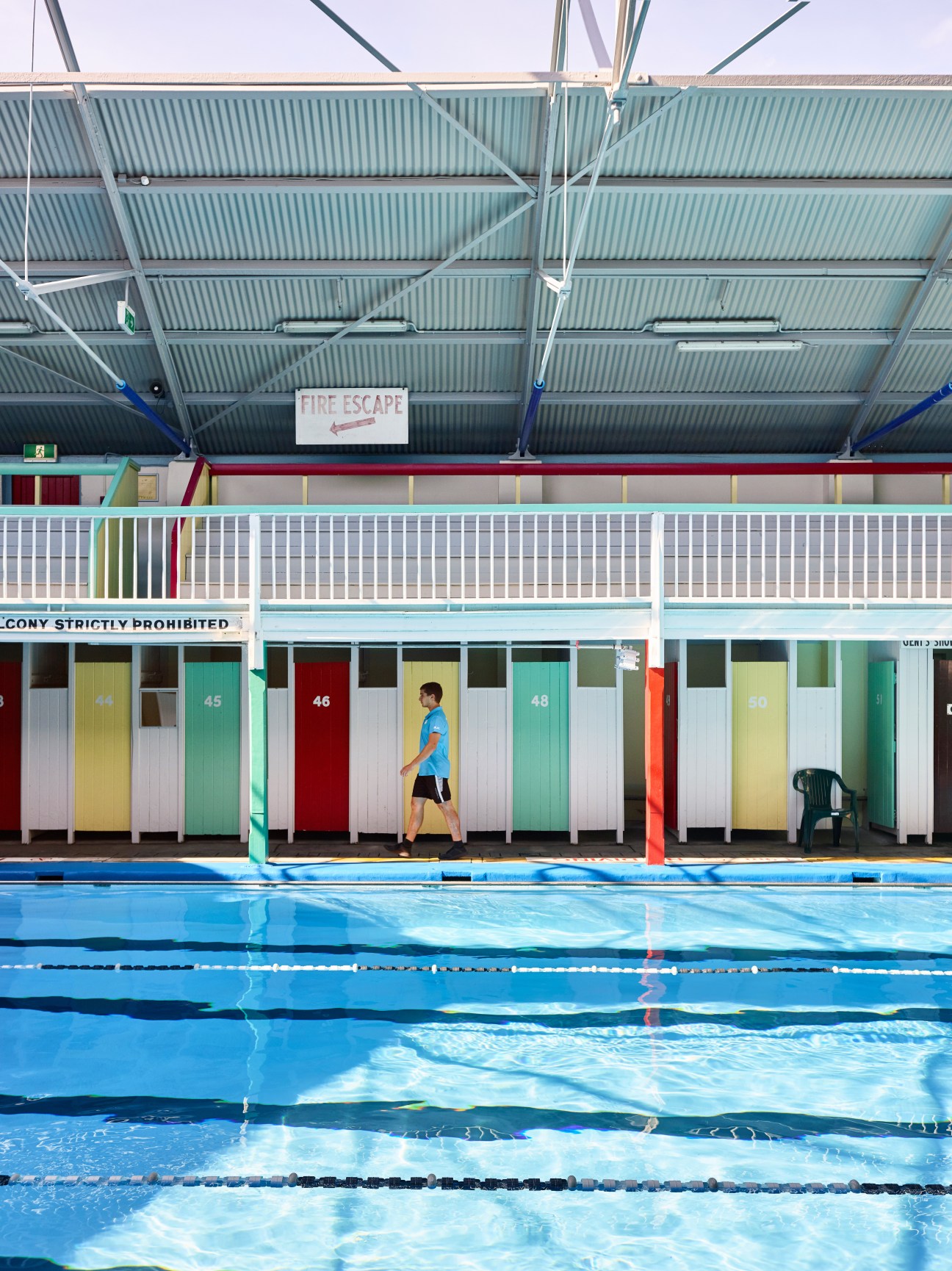 Colorful changing room cubicles at an indoor swimming pool facility with numbered doors and metal railings.