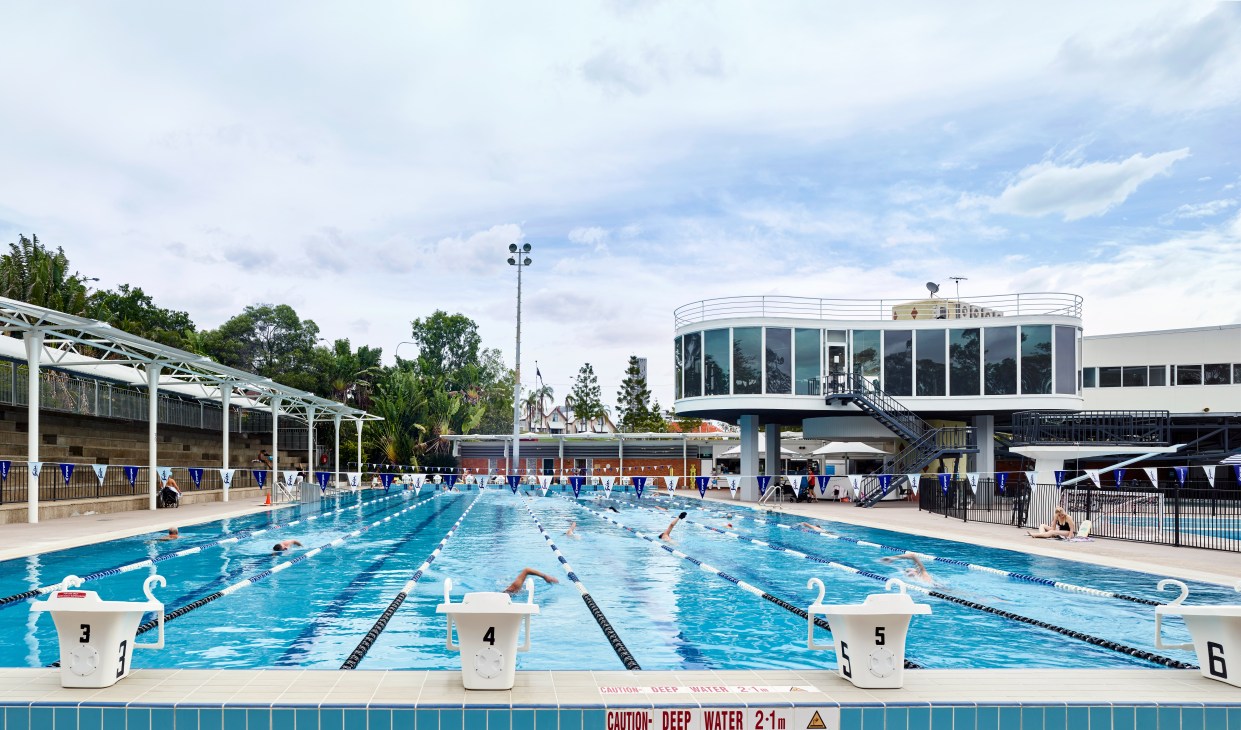 Swimmers training in lanes at Centenary Pool in Brisbane with a modernist cylindrical building and gym complex visible in the background.