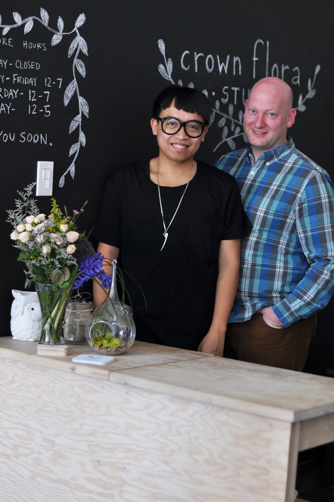 Textile artist Davis Khounnoraj and florist Adam Mallory stand behind a wooden counter at Crown Flora Studio in Toronto.