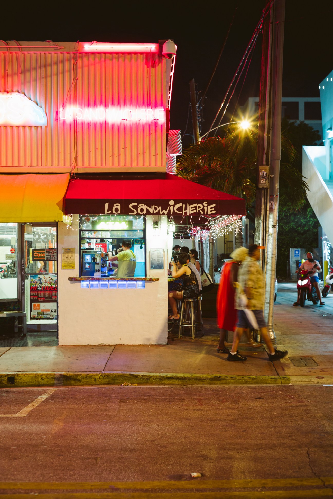 La Sandwicherie storefront in Miami with neon red signage at night and pedestrians outside.
