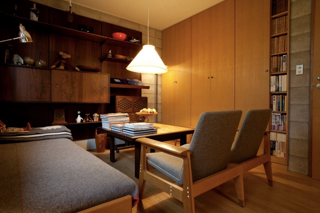 Guest room with wooden Finn Juhl wall system, sofa, chairs, pendant lamp, bookshelves and minimal Scandinavian furniture.