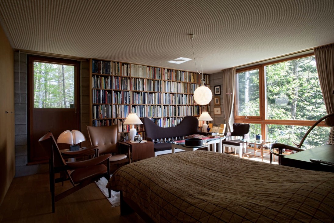 Bedroom with Finn Juhl furniture, bookshelves, and forest views through large windows.