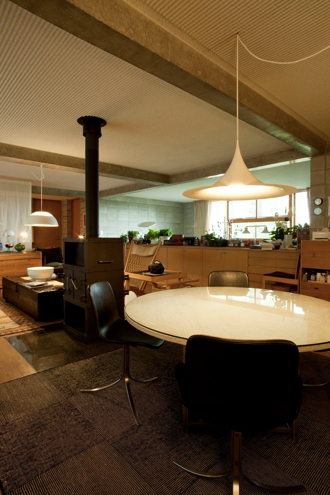 Mid-century modern dining room with round white table, black leather chairs, pendant lighting, and black stove.
