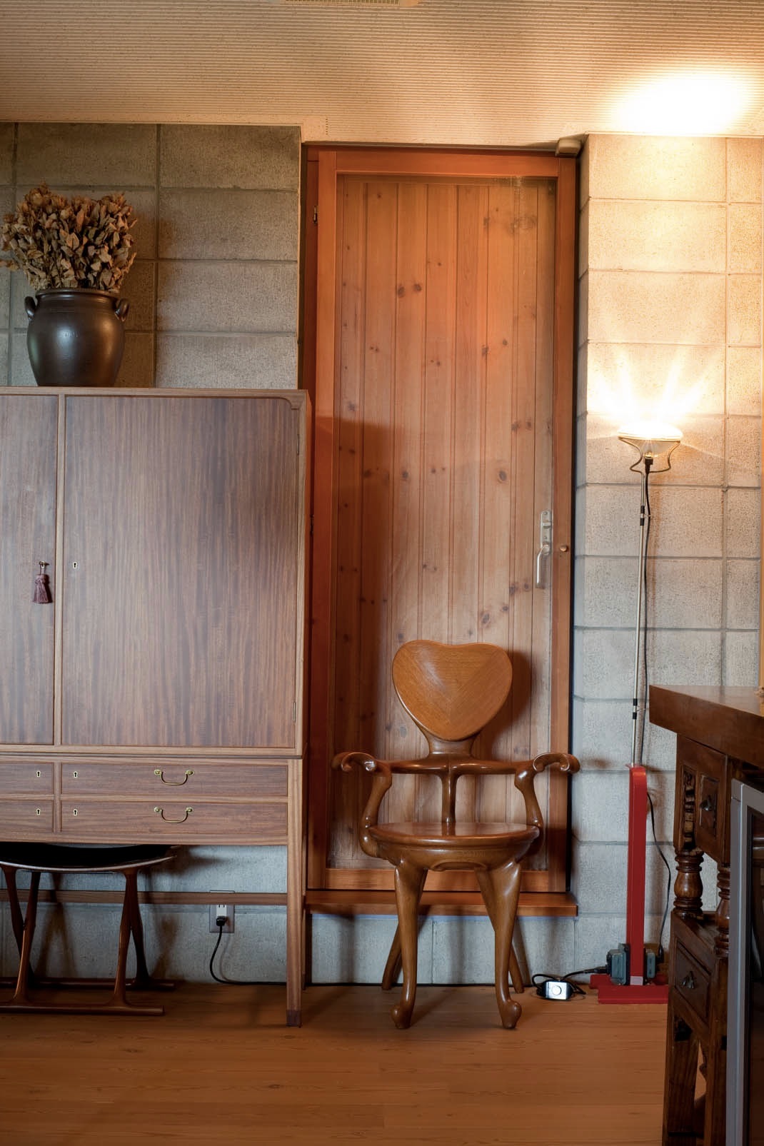 Wooden cabinet with a heart-shaped chair by Antonio Gaudi positioned in front of a wooden door.