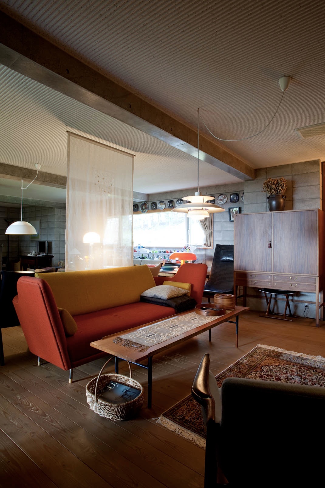 Mid-century living room with red and yellow Finn Juhl sofa, wooden table, and pendant lighting.
