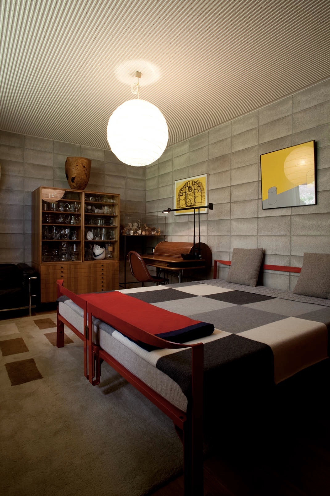 Bedroom with red bed frame, wooden desk, storage cabinet, and globe pendant light under corrugated ceiling.