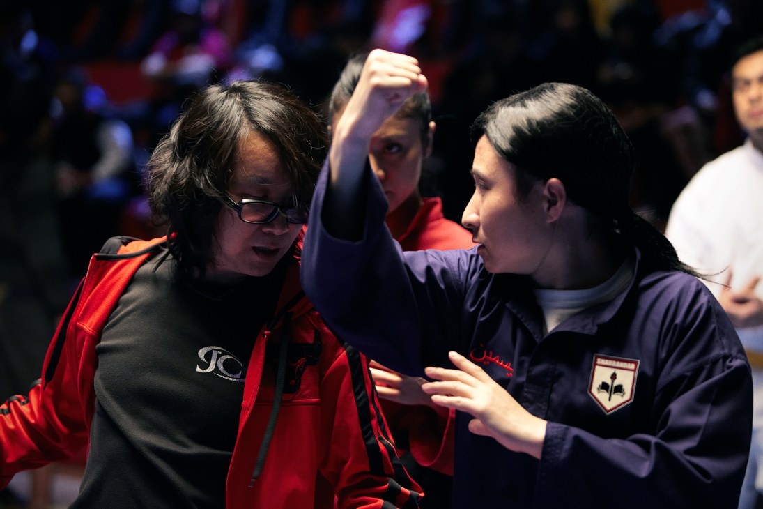 Chan Man-Ching, wearing glasses and a red jacket, demonstrates a martial arts move on set during Brunei's first commercial feature film.