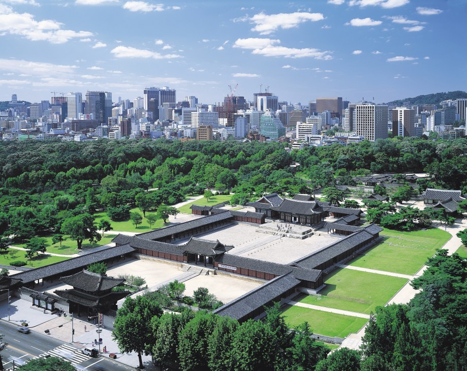 Changdeokgung Palace in Seoul with traditional Korean architecture surrounded by green gardens, overlooking modern city skyline.