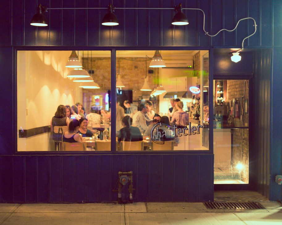 Chantecler restaurant storefront at night with illuminated windows showing diners inside and neon signage.