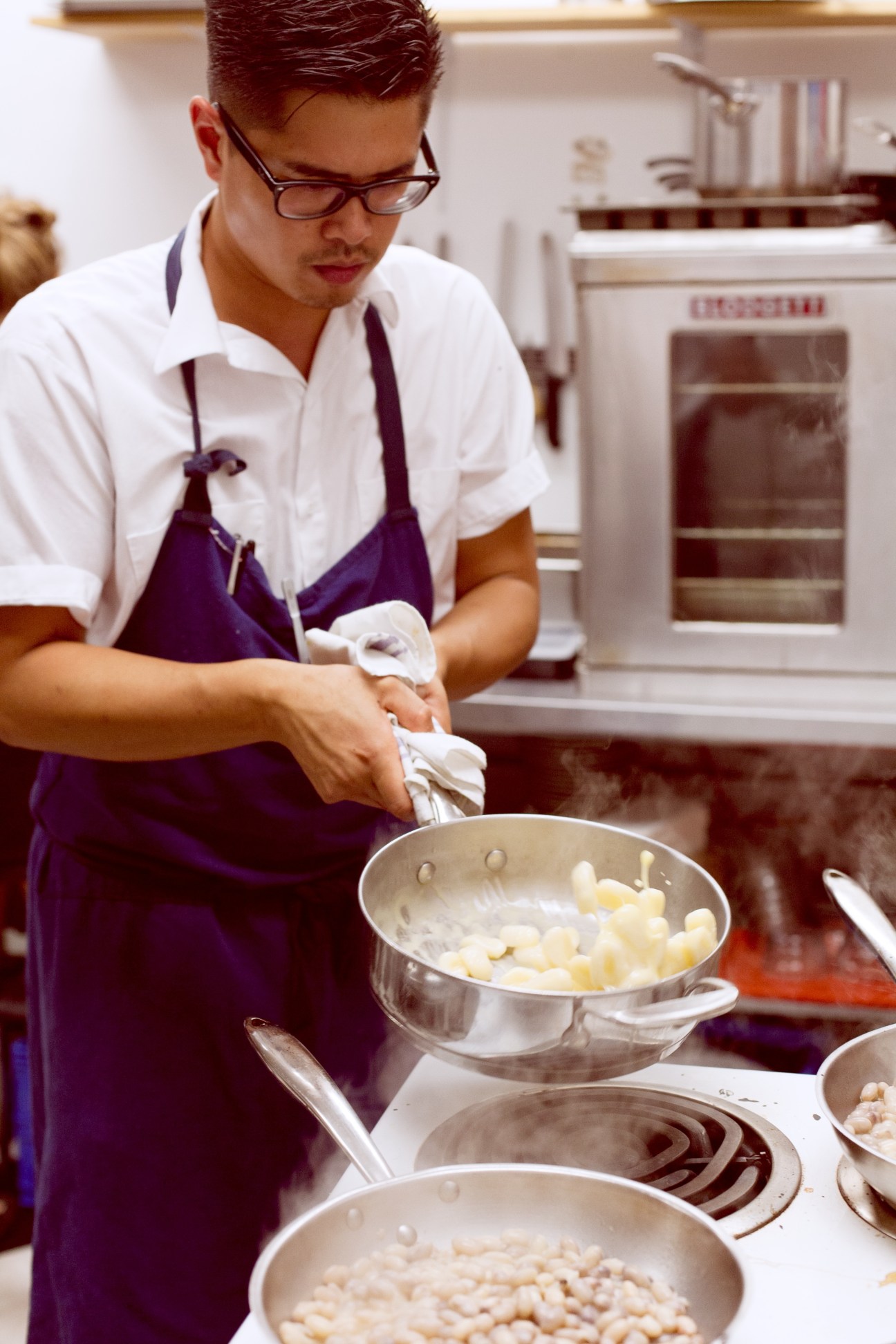 Chef Jonny Poon wearing glasses and purple apron prepares food in a kitchen at Chantecler restaurant.