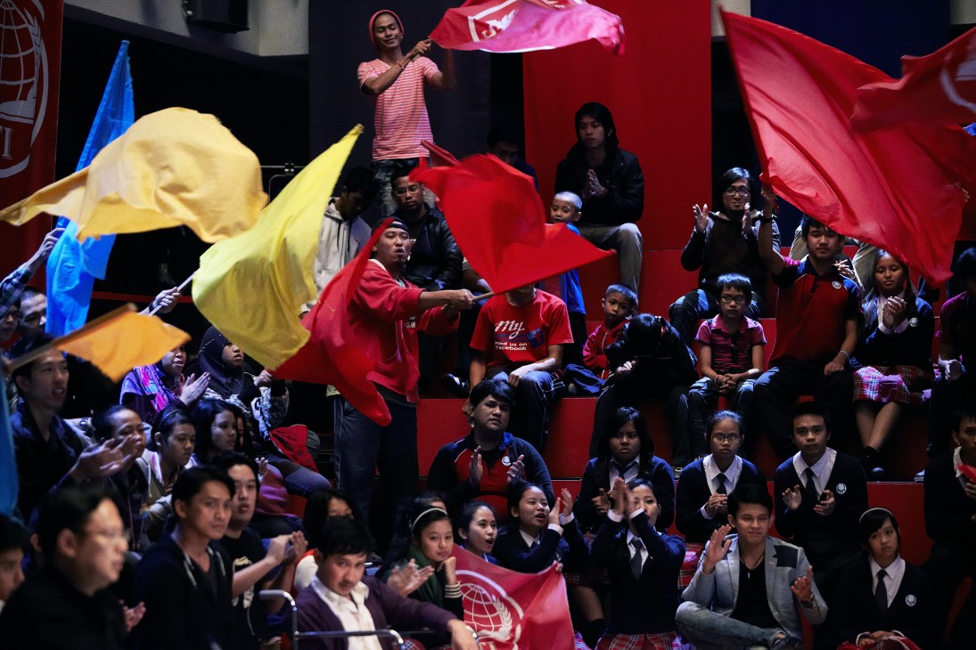 Large crowd of extras holding colorful flags and umbrellas during a scene filmed in an auditorium for Brunei's first commercial feature film.