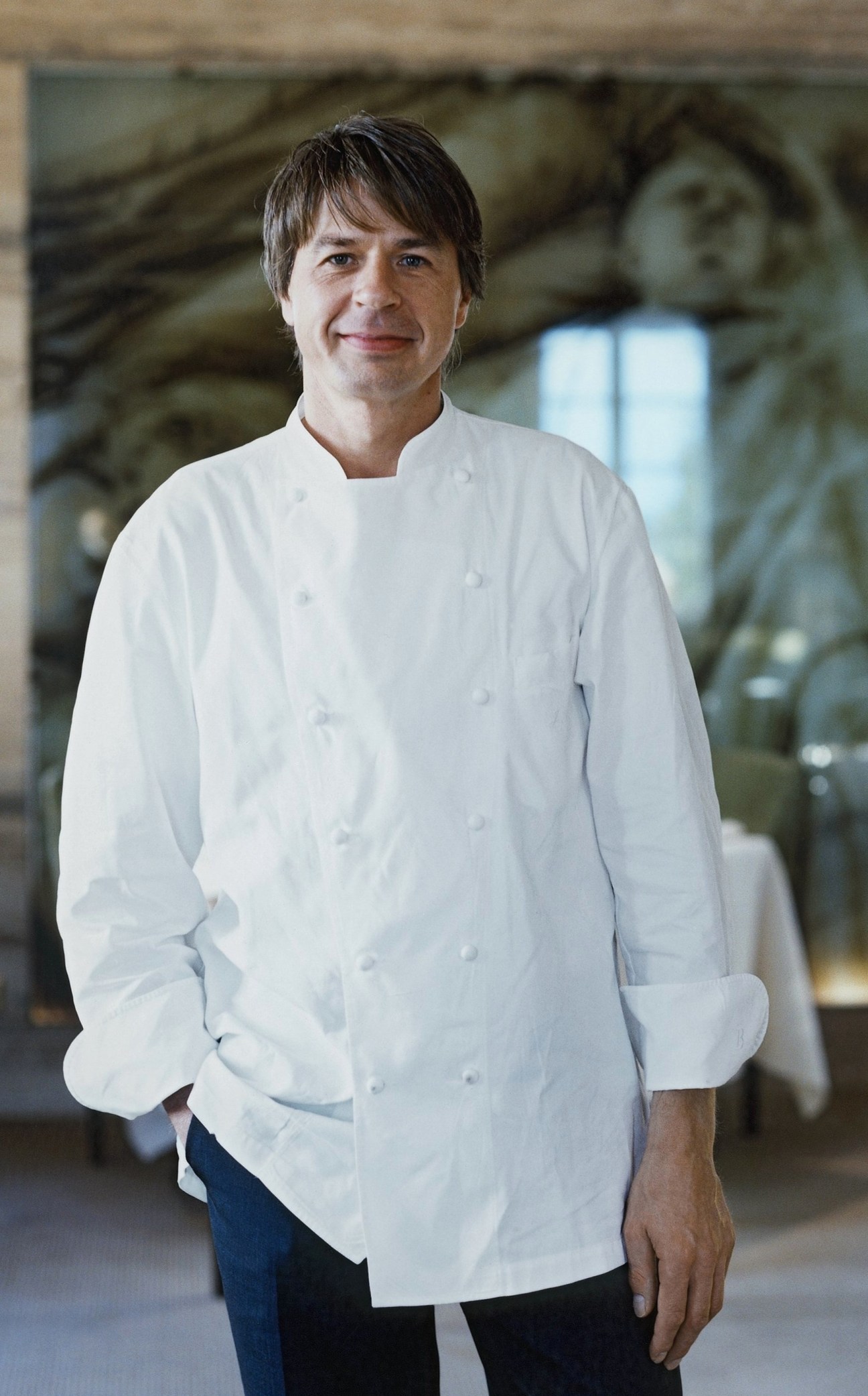 Chef Joachim Wissler in white chef's coat standing in an ornate restaurant interior.