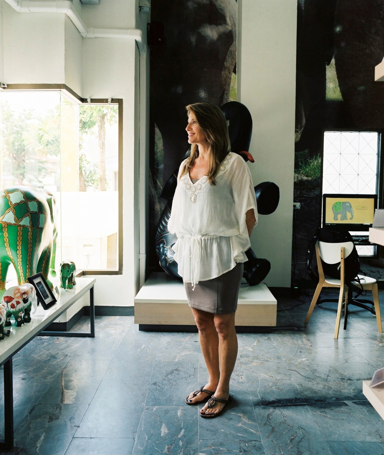 Ann Healy, general manager at Elephant Parade, stands in a gallery space with artwork displayed on walls.