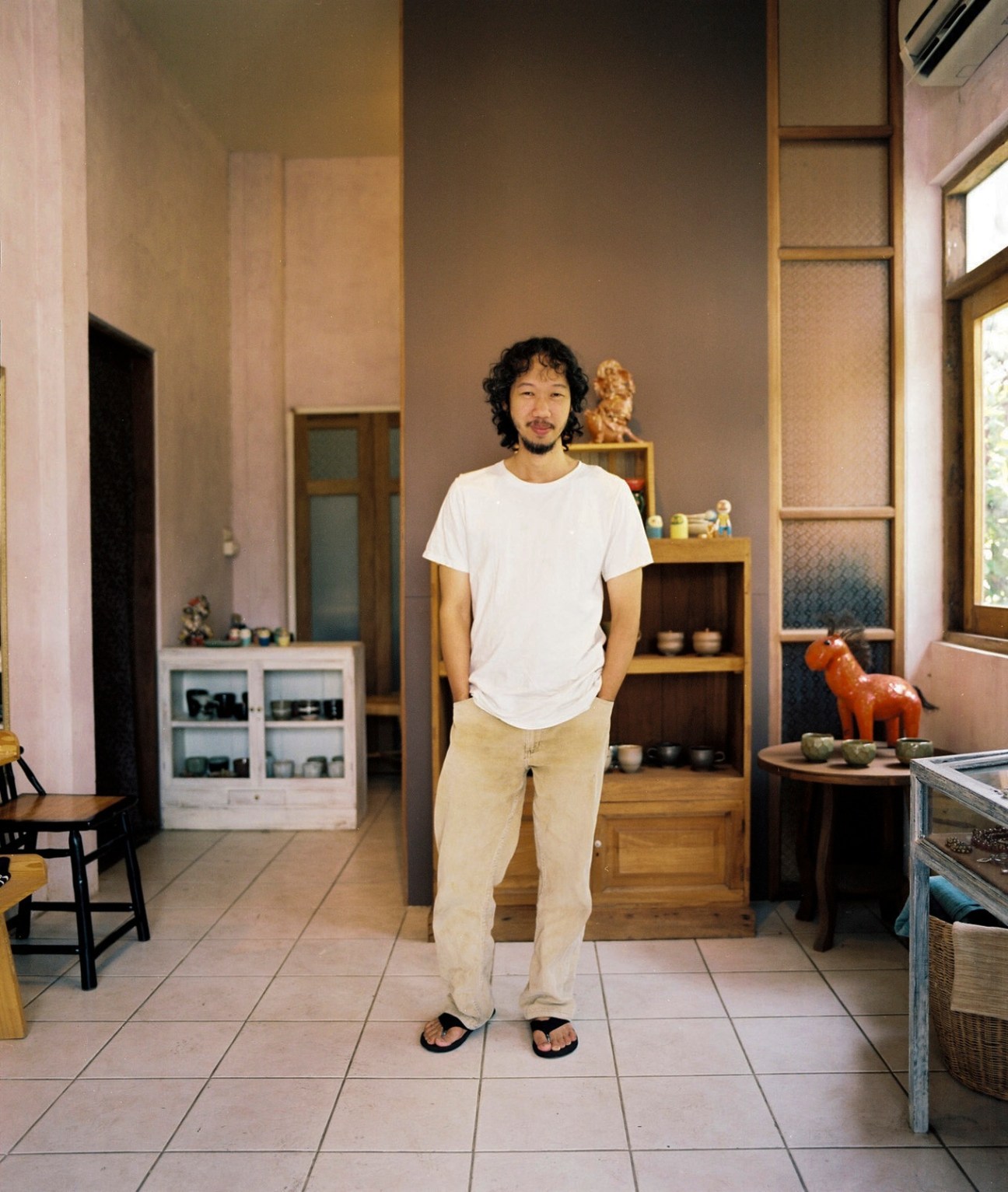 Man standing in a minimalist gallery space with warm-toned walls and wooden shelving displays.