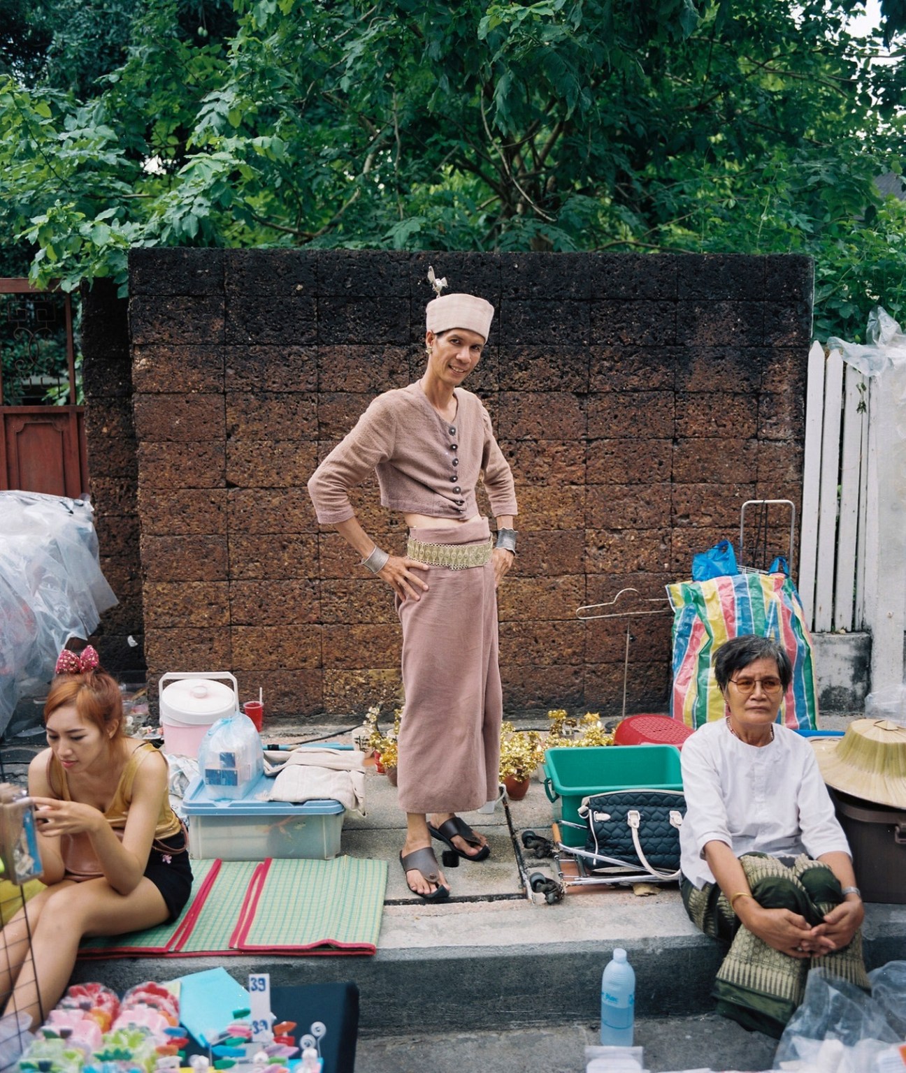 Local street seller in traditional tan clothing posing in front of his market stall in Chiang Mai.