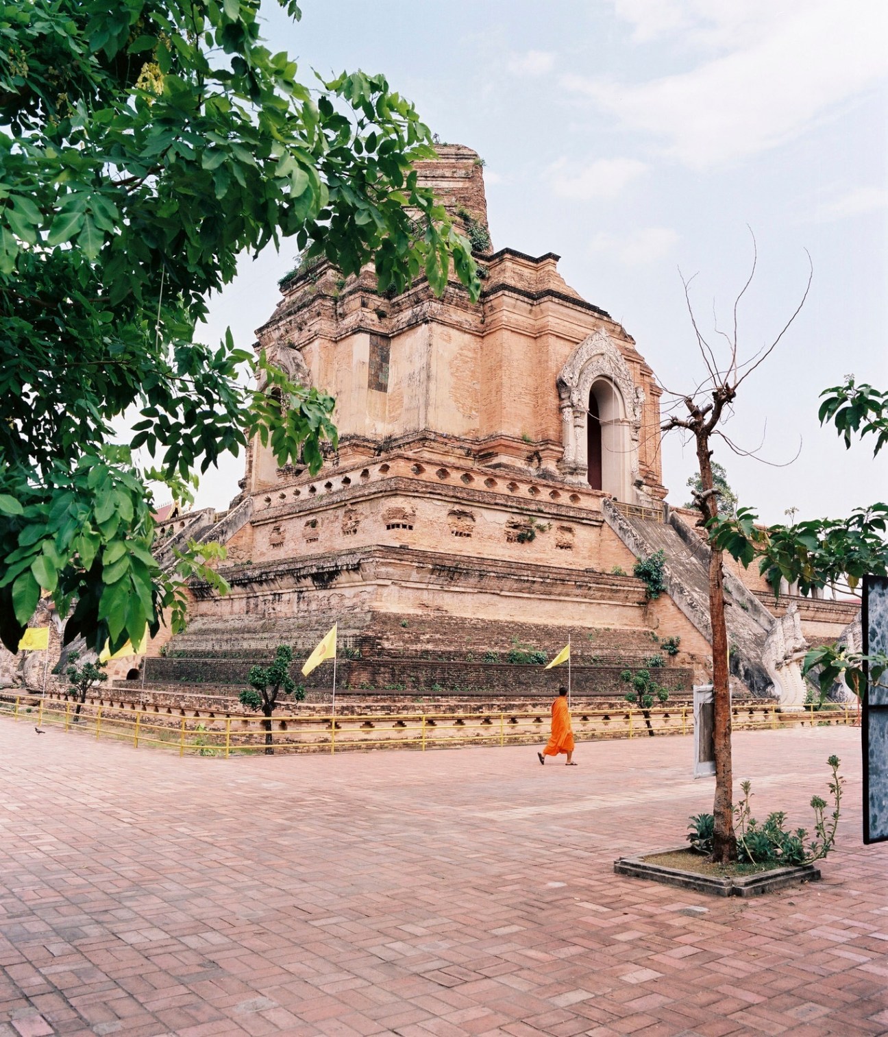 Wat Chedi Luang temple in Chiang Mai with a monk walking across the brick plaza.