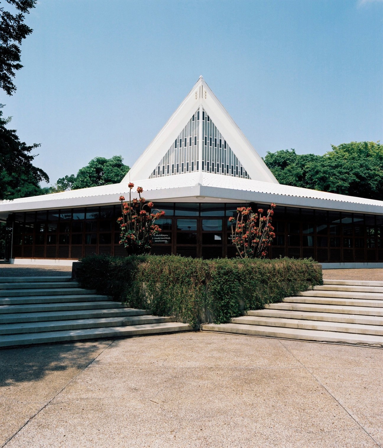 White postmodern church building with triangular roof and vertical window slats, surrounded by green landscaping.