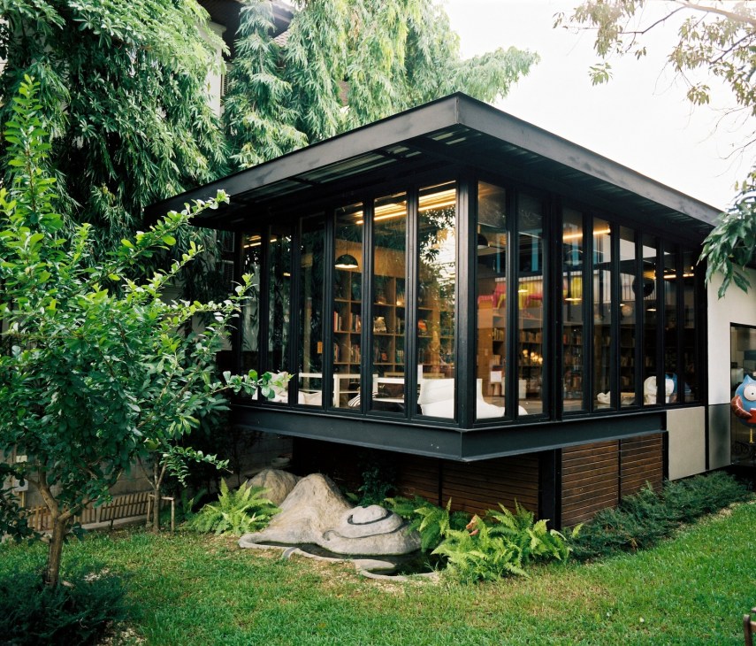 Modern black-framed building with glass walls surrounded by lush green vegetation and landscaping.