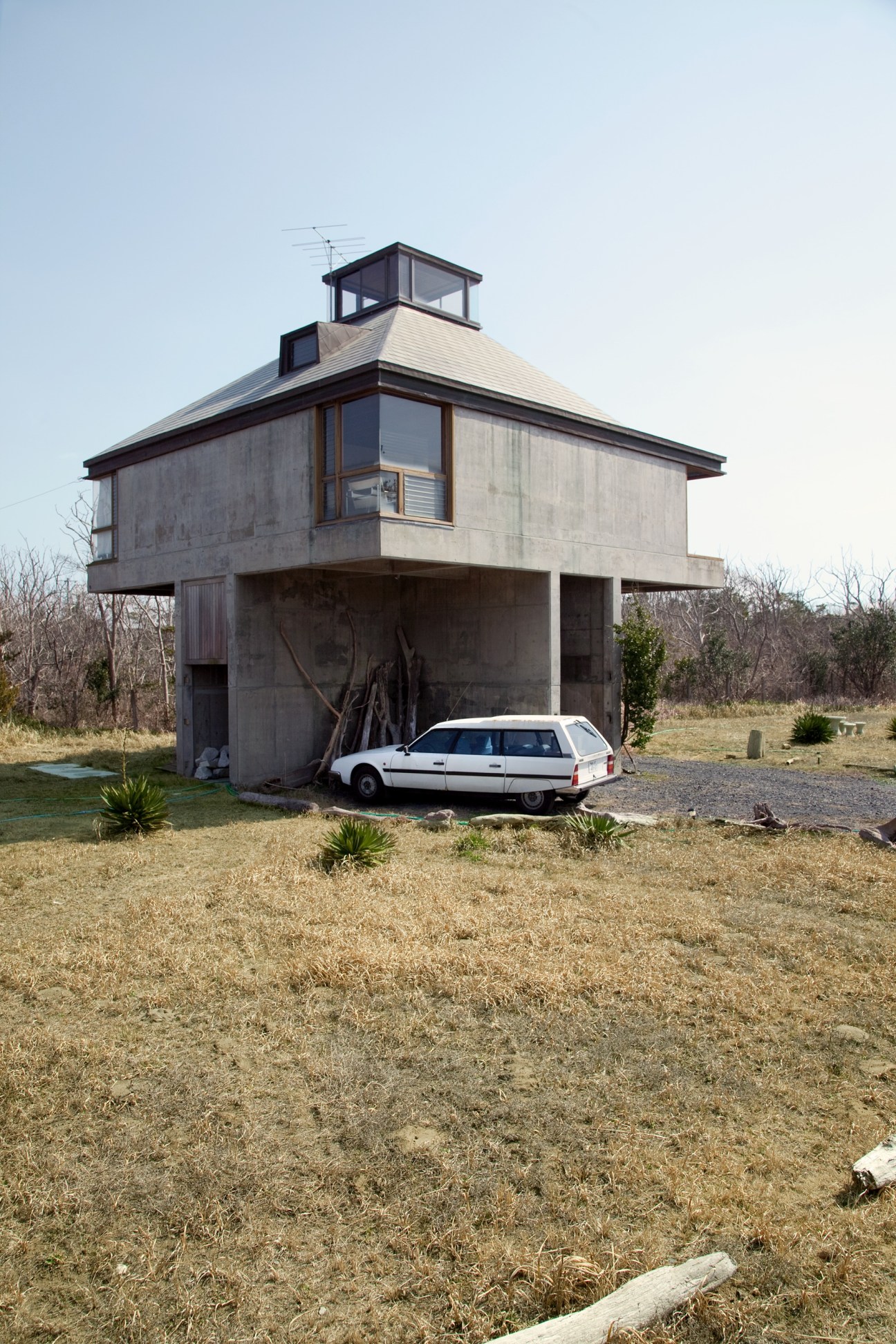 Modern concrete and wood house with elevated design near Chiba Beach, featuring a white car parked underneath.