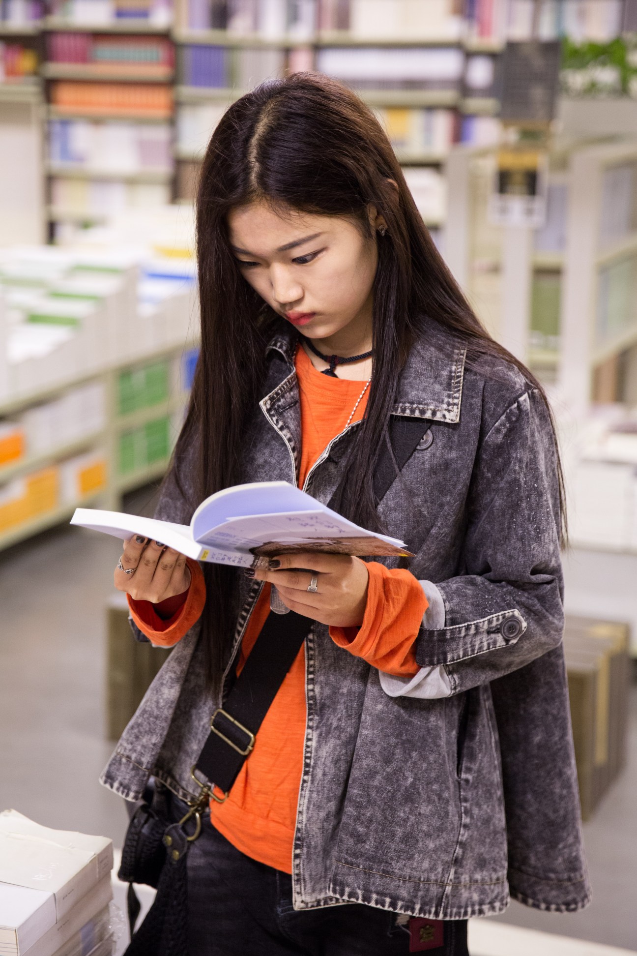 Young woman reading a book in a bookshop with shelves of books blurred in the background.
