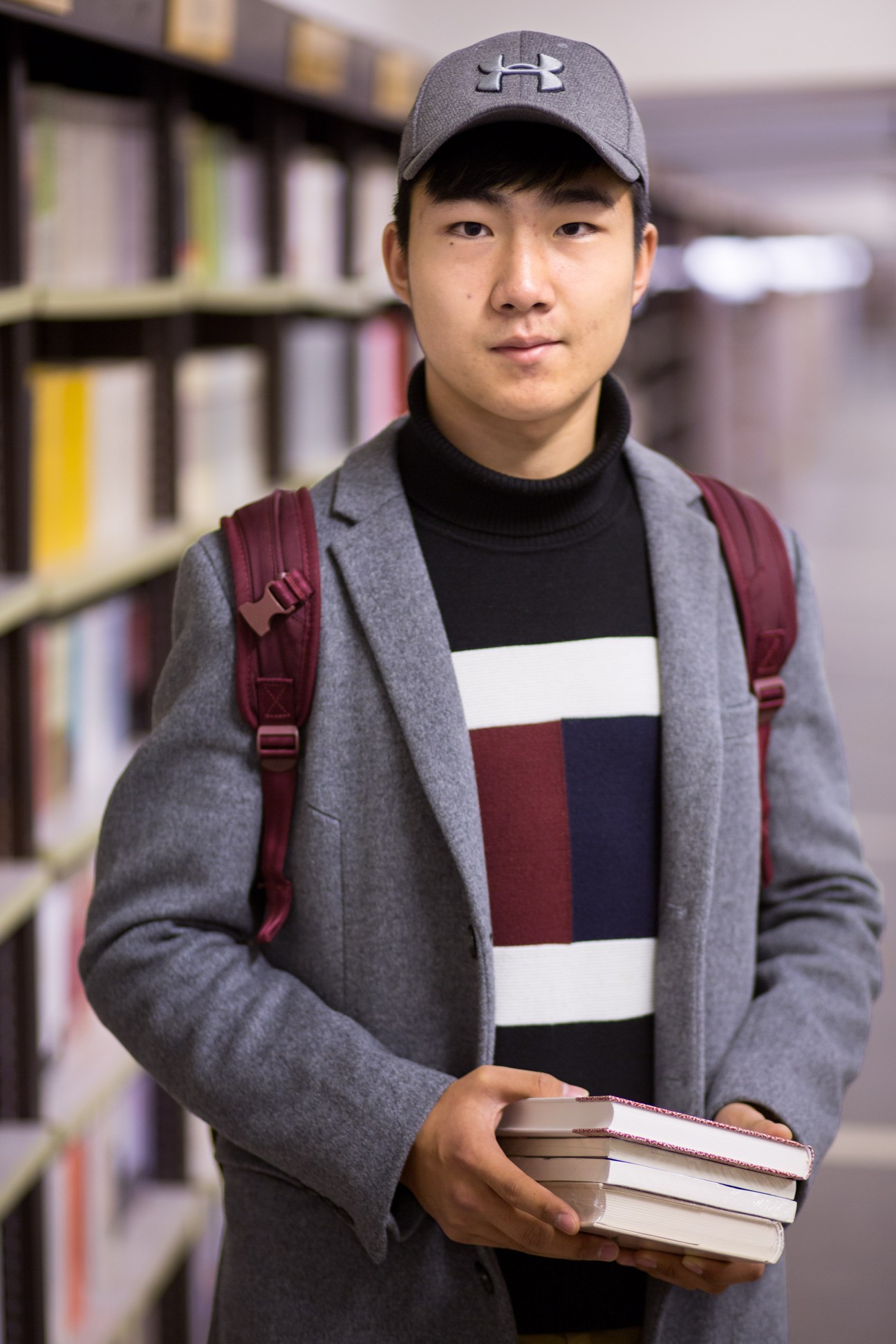 A young person holding a stack of books stands in front of bookshelves at Librairie Avant-Garde bookshop.