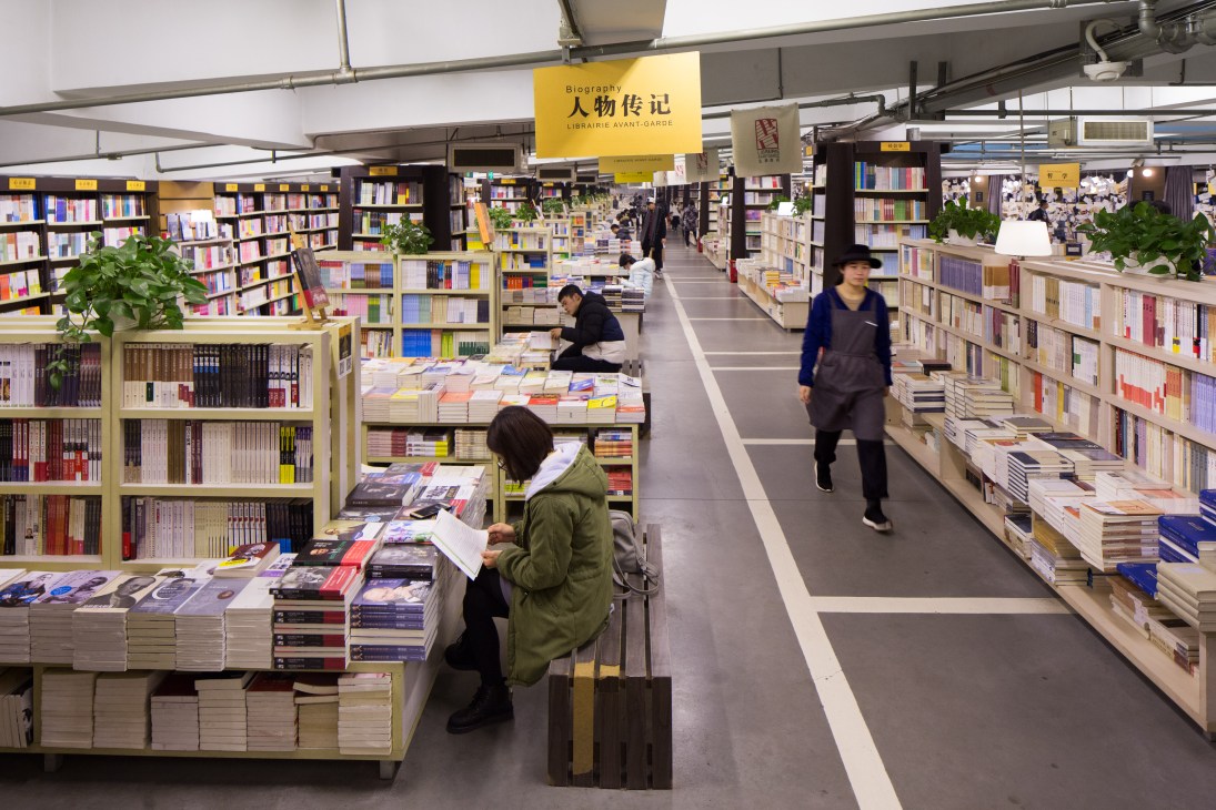 Interior of Librairie Avant-Garde bookstore in Nanjing with extensive shelving, yellow signage, and customers browsing books.