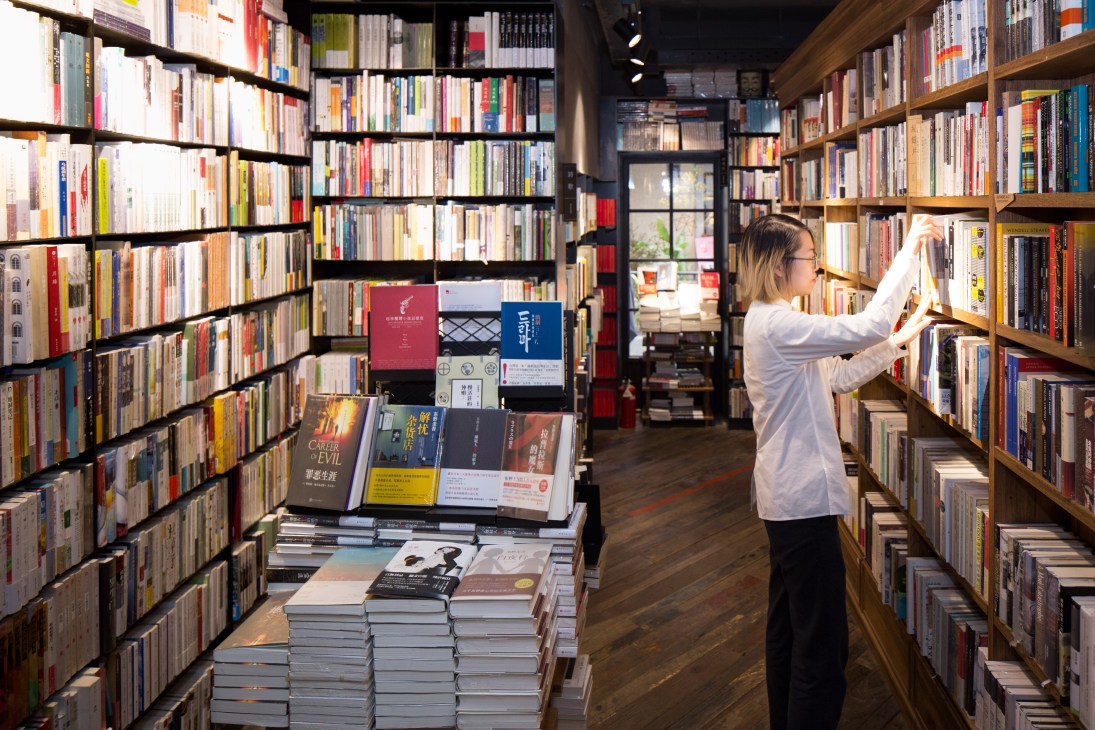 Customer browsing books on wooden shelves at The Mix Place bookshop in Shanghai.