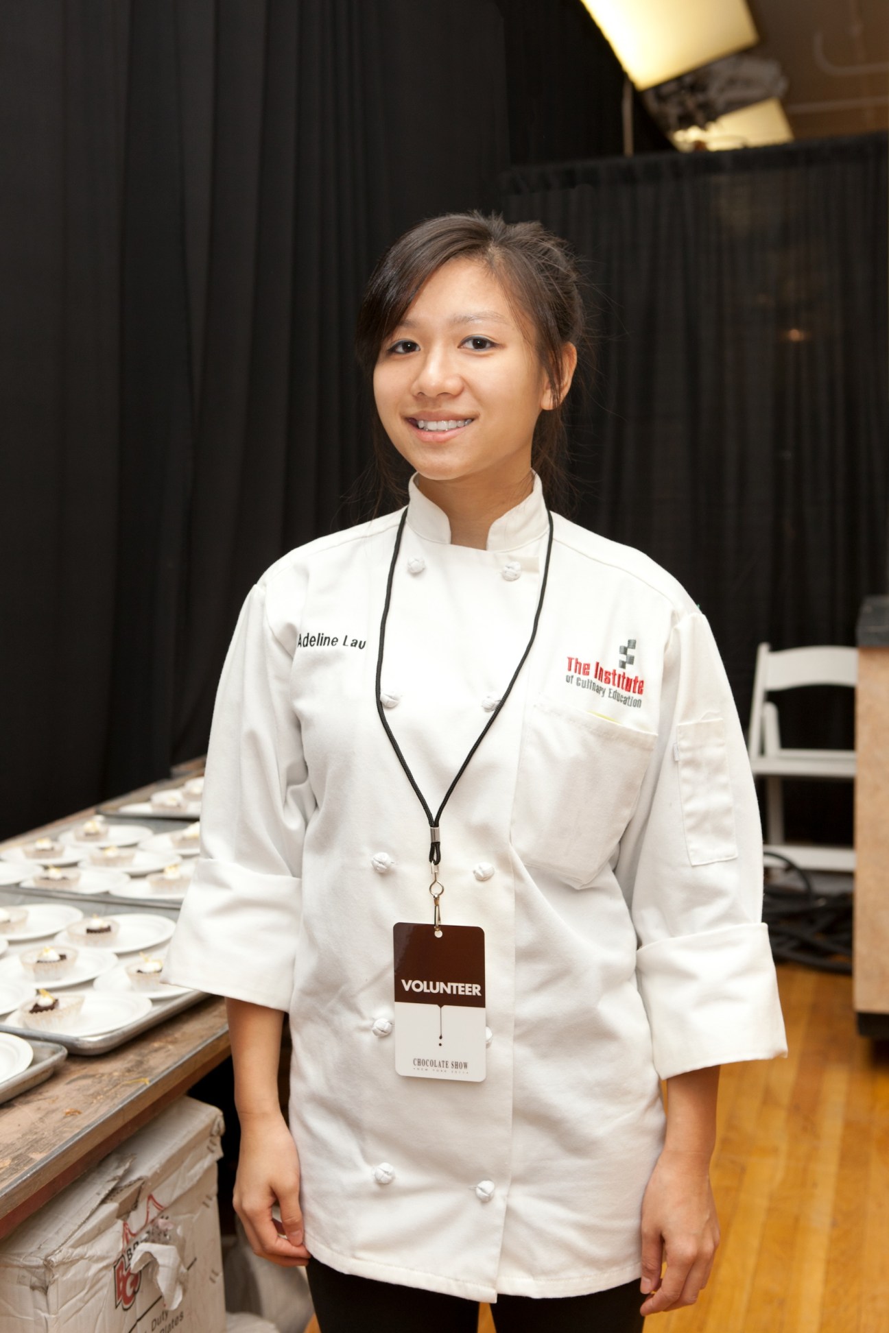 Adeline Lau, a Chocolate Fair volunteer, wearing a white chef's coat and volunteer badge.