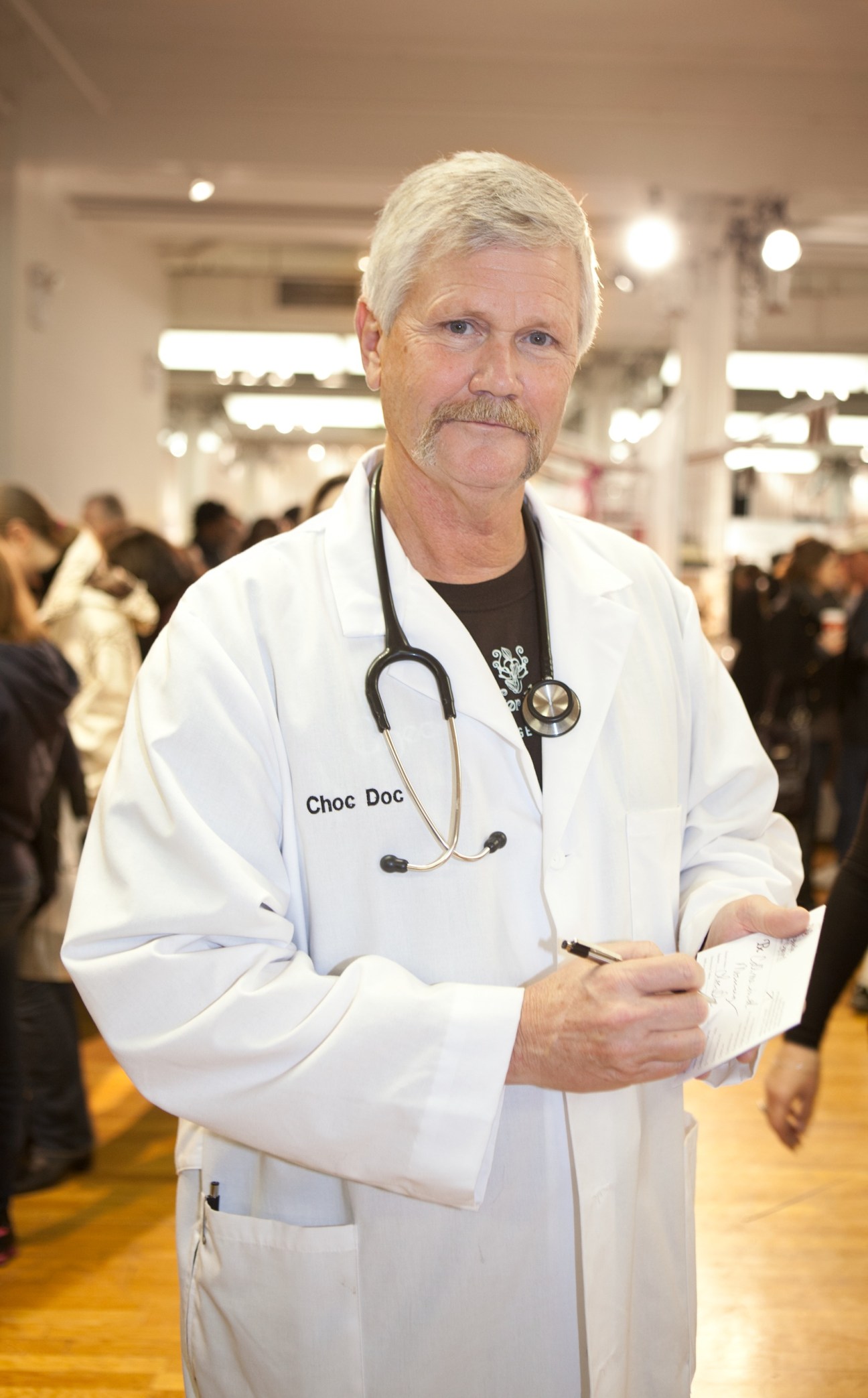 A man dressed as a doctor with a stethoscope and white coat labeled 'Choc Doc' at the New York Chocolate Show.
