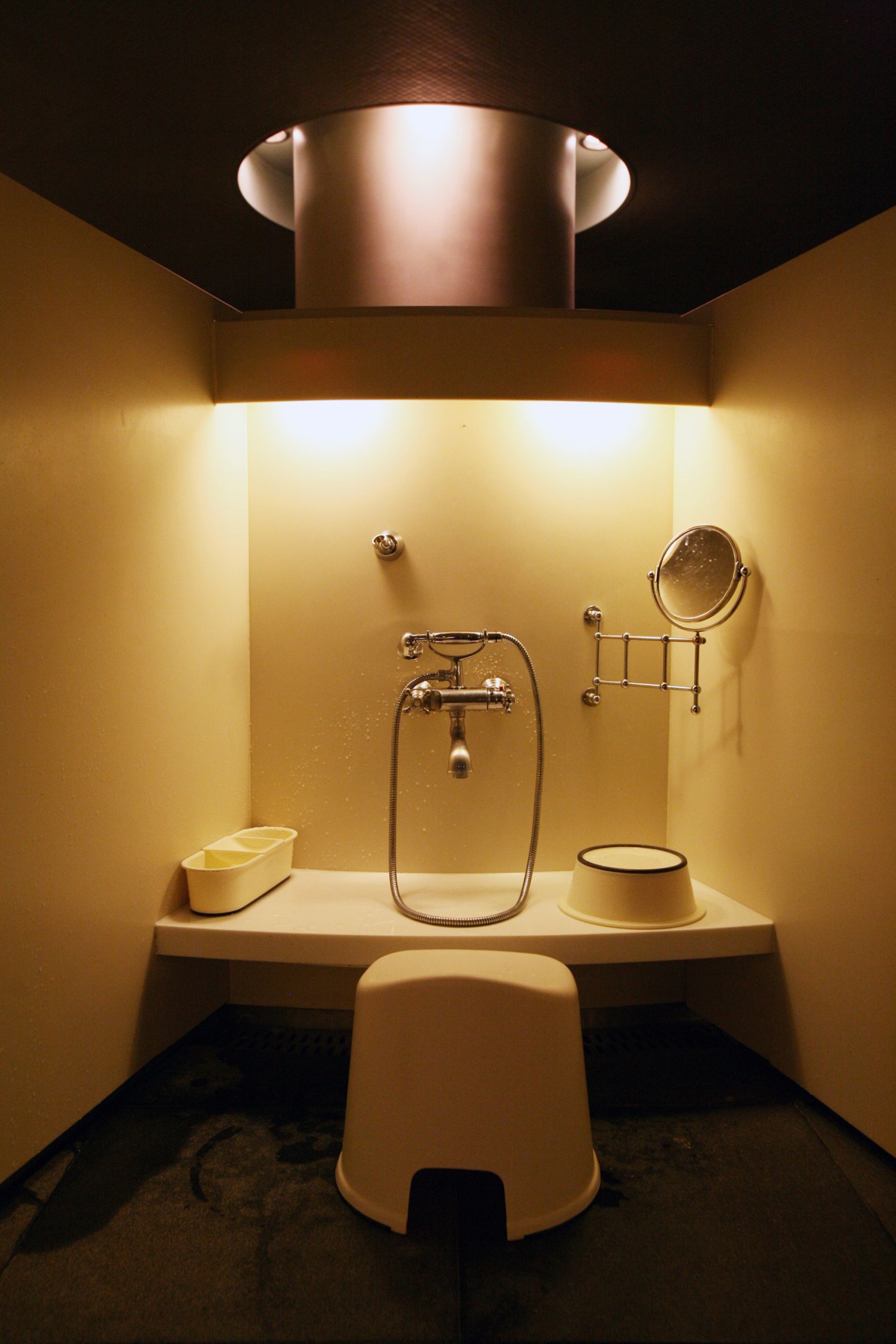 Modern spa bathroom with cream-colored fixtures, mirror, and hand shower against warm yellow walls.